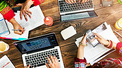 Foto von Händen die auf Papier und Laptops arbeiten