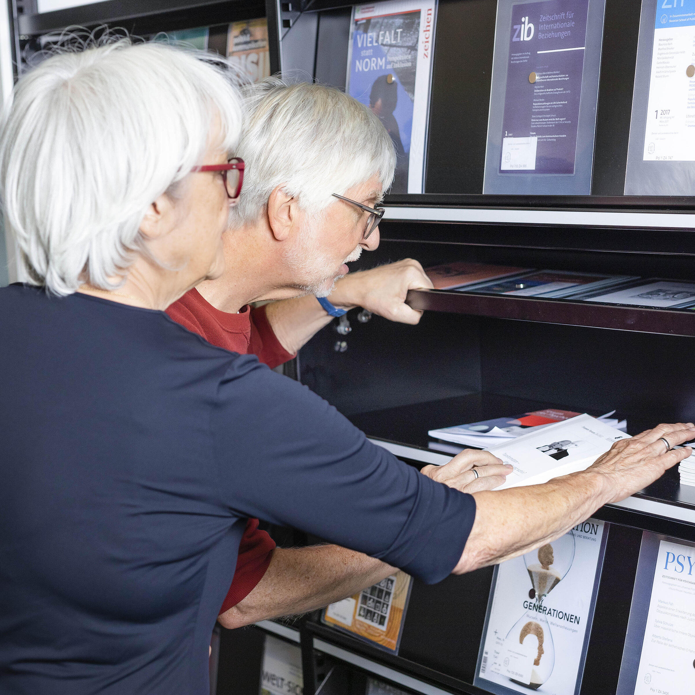 Two elderly people look into a magazine compartment in the lounge of the AGB