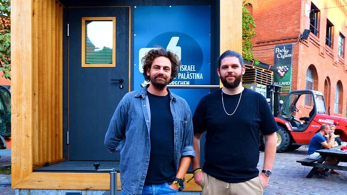 Shai Hoffmann und Zakariyya Meißner stehen vor einem Tiny House. 