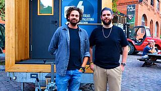 Shai Hoffmann und Zakariyya Meißner stehen vor einem Tiny House.
