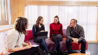 Foto von vier Personen, die sich sitzend unterhalten