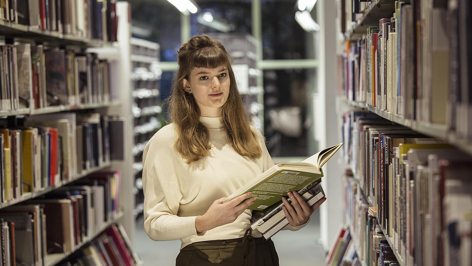 Young woman with stack of books in hand stands in the AGB