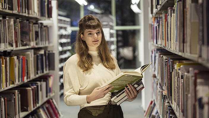 Young woman with stack of books in hand stands in the AGB