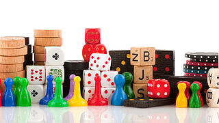 Verschiedene Spielfiguren, Chips und Würfel vor einem weißen Hintergrund