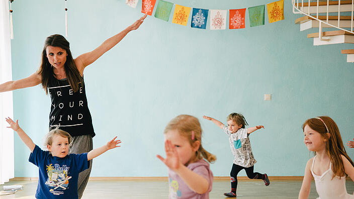 vier Kinder tanzen im Raum verstreut in Begleitung einer Frau durch den Raum