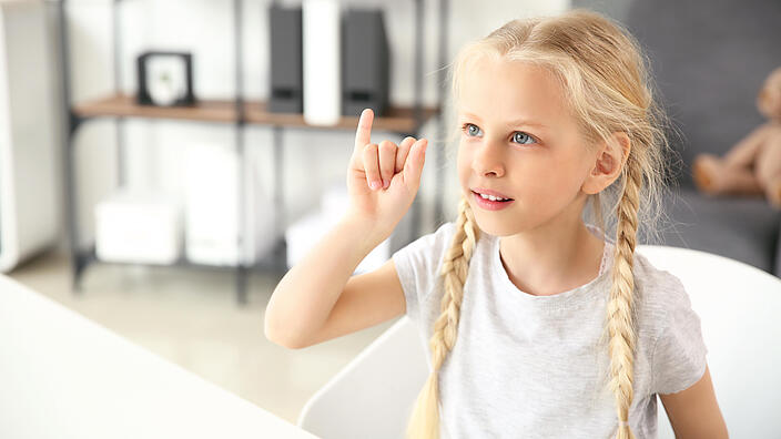 Kind macht Zeichensprache mit Hand.