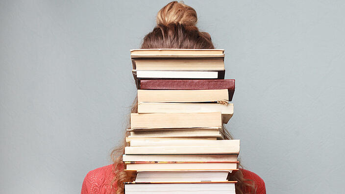 Frau hält Bücherstapel vor Ihrem Körper inklusive dem Gesicht