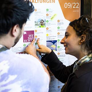 Zwei Menschen zeigen auf einen bunten Veranstaltungskalender mit kostenlosen Veranstaltungen in Berlin