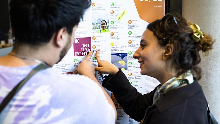 Zwei Menschen zeigen auf einen bunten Veranstaltungskalender mit kostenlosen Veranstaltungen in Berlin