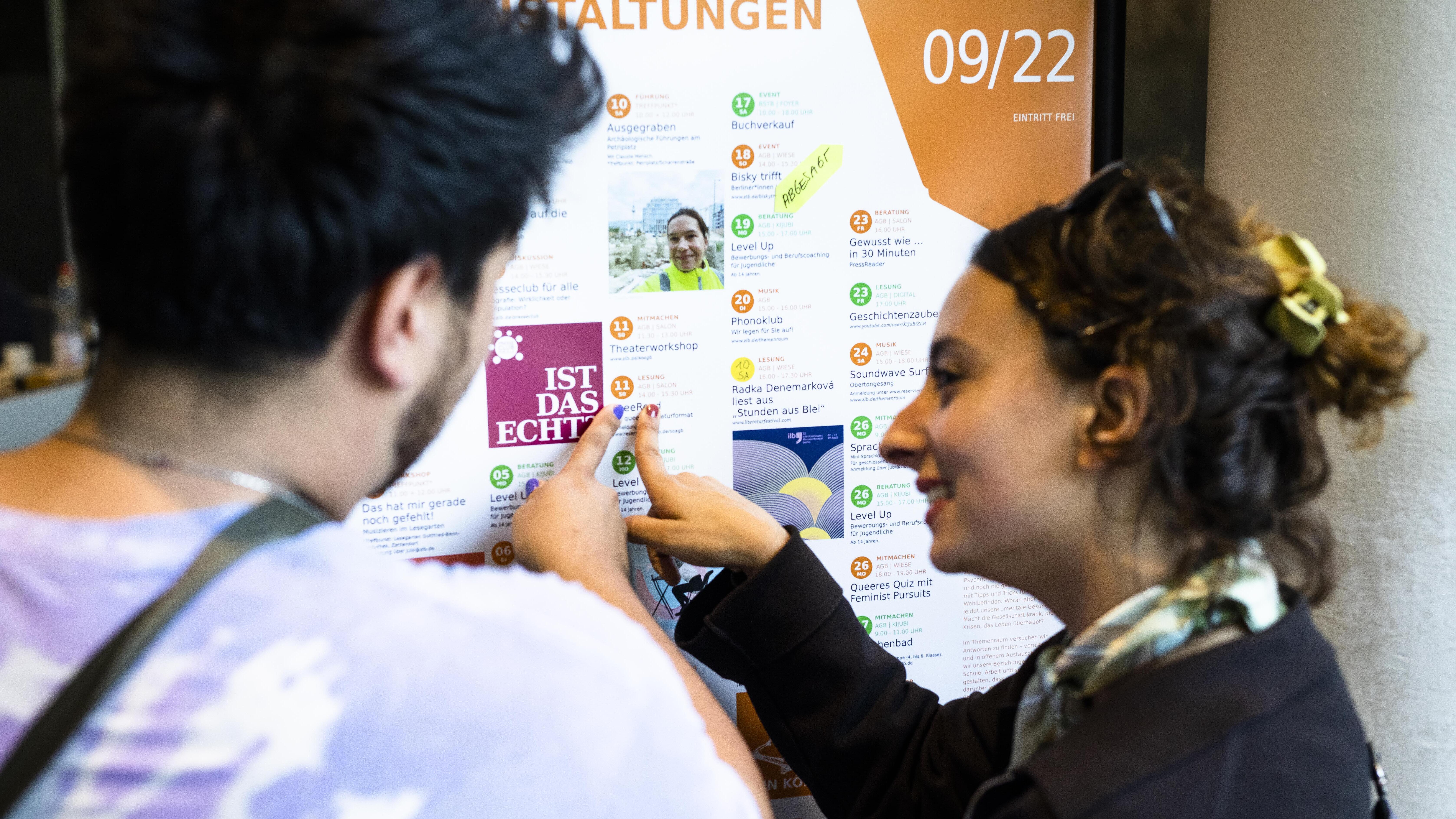 Two people point to a colorful calendar of free events in Berlin
