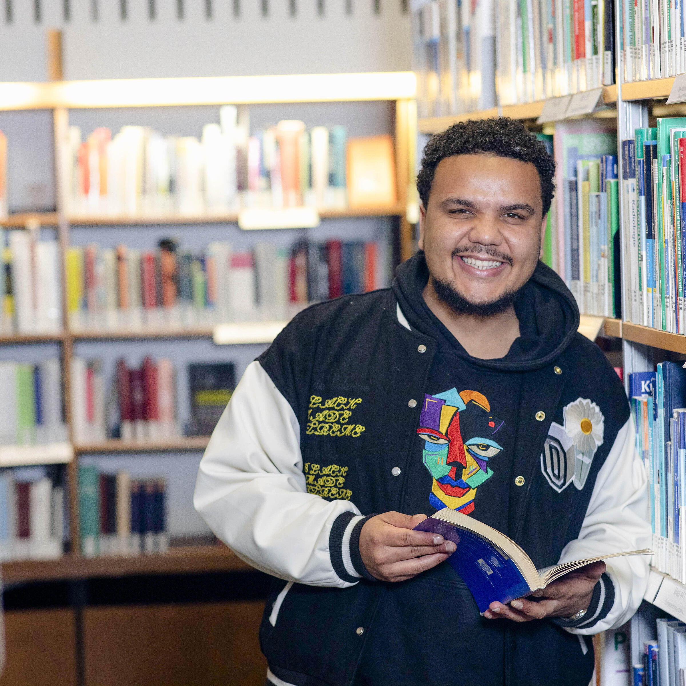 Junger Mann steht mit aufgeschlagenem Bestseller Sachbuch vor Regal in Berliner Stadtbibliothek