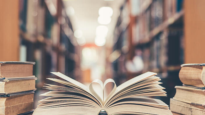 Aufgeschlagenes Buch in Bibliothek, bei dem zwei Seiten eine Herzform darstellen
