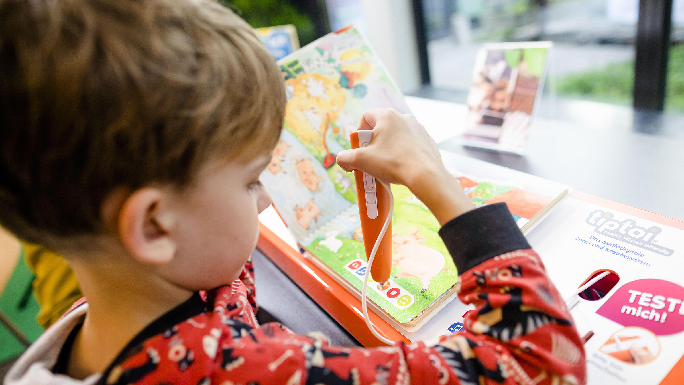 Junge drückt mit Tiptoi-Stift auf Symbol in Tiptoi-Buch in Bibliothek