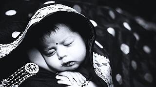 Eine Kind schläft friedlich bis über den Kopf mit einer Decke zugedeckt.