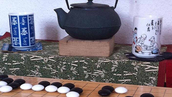 Eine Teekanne mit Tassen und davor ein Go Spiel.