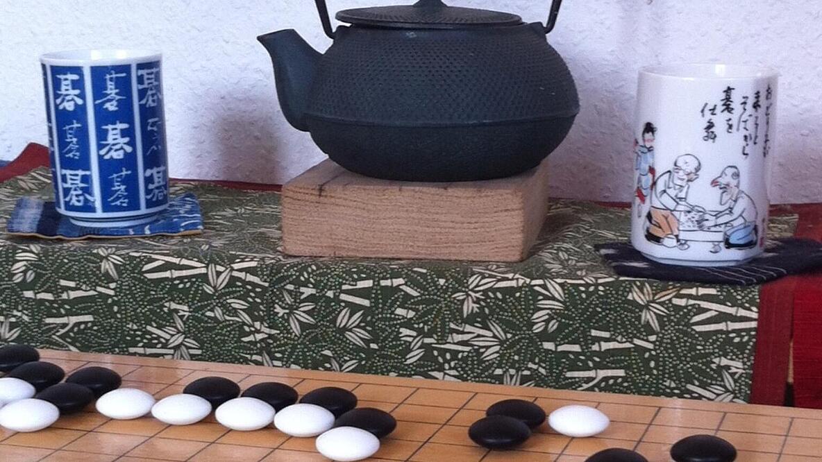 Eine Teekanne mit Tassen und davor ein Go Spiel.