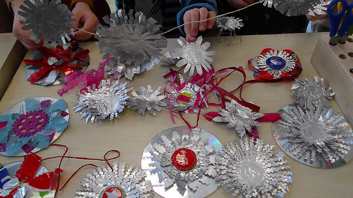 mehrere Kinderhände basteln Objekte aus CD´s, Alufolie, Kronenkorken und anderen recycelten Materialien