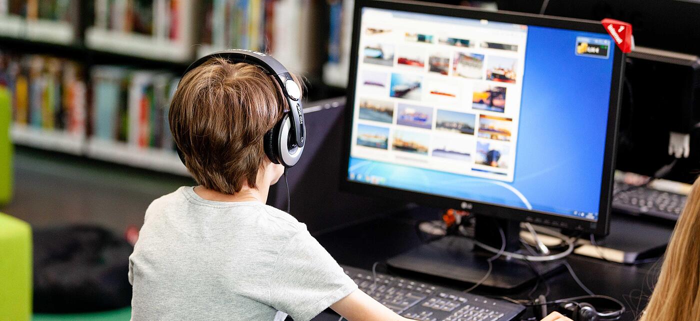 Junge sitzt mit Kopfhörern vor einem Computerbildschirm