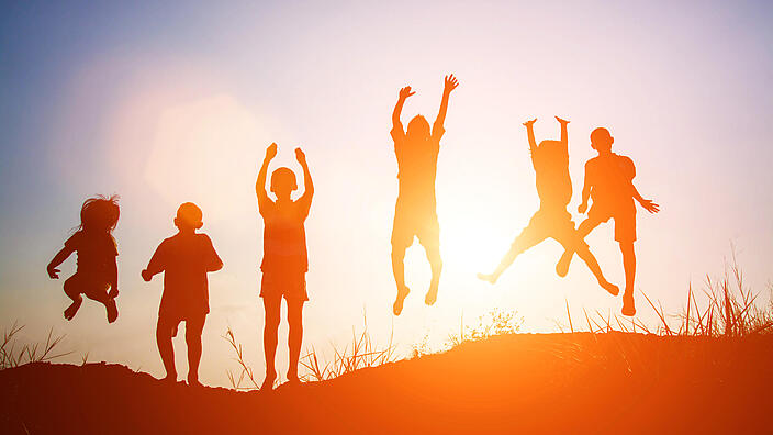Silhouetten von sechs Kindern in Sommerkleidung, die in die Luft springen