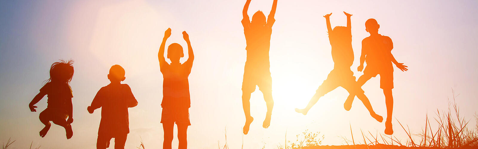 Silhouetten von sechs Kindern in Sommerkleidung, die in die Luft springen