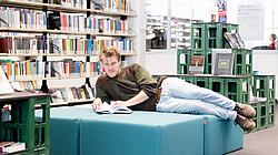 Ein Mann liegt auf gepolsterter Bank in Bibliothek und liest in Buch