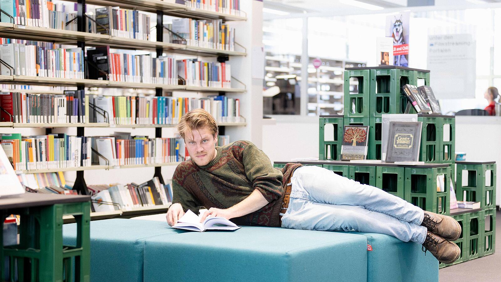Ein Mann liegt auf gepolsterter Bank in Bibliothek und liest in Buch