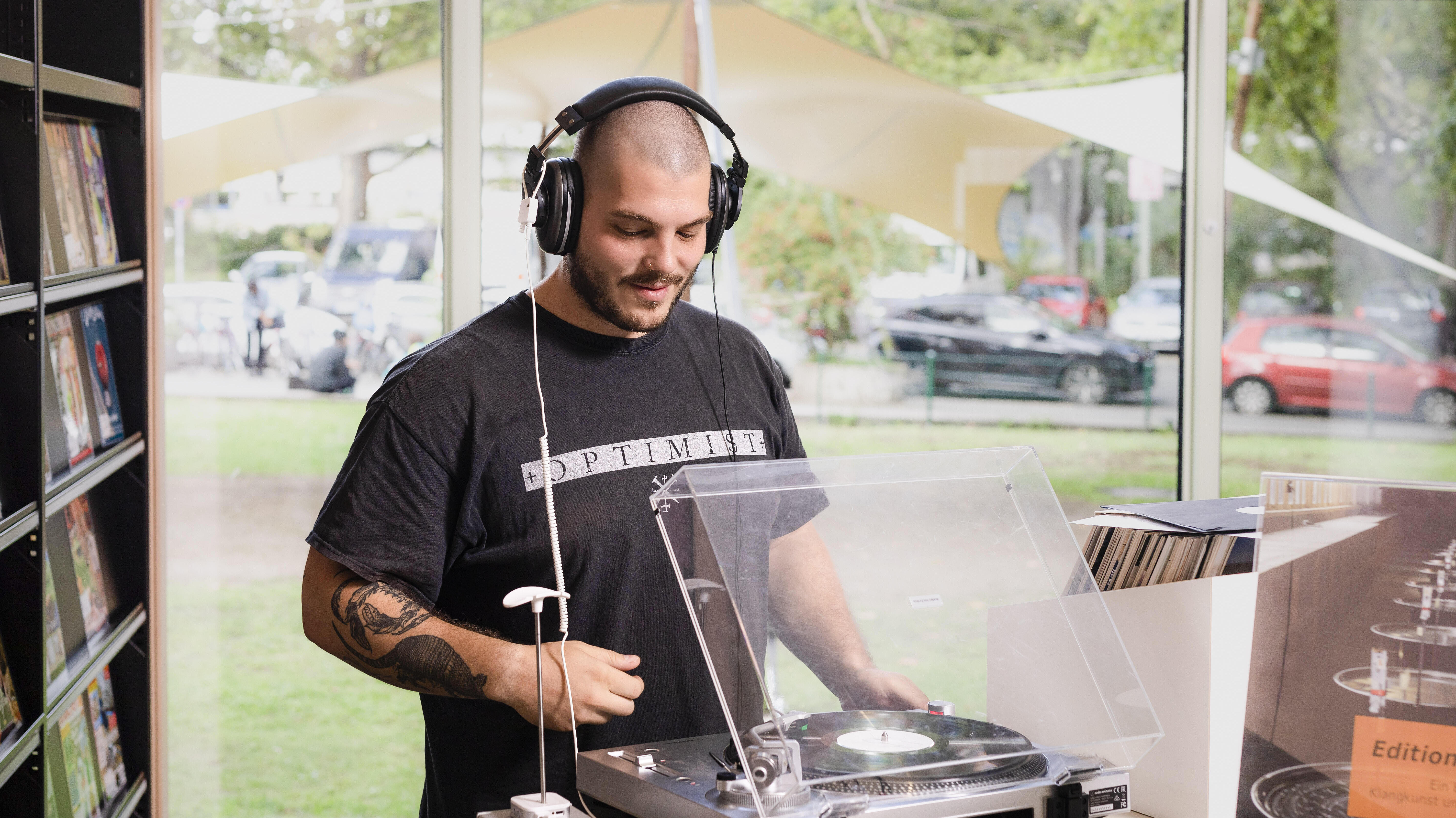 DJ mit Kopfhörern steht an Plattenspieler in Bibiothek
