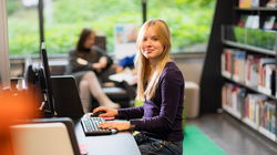 Jugendliches Mädchen sitzt an PC und hat Hände auf Tastatur.