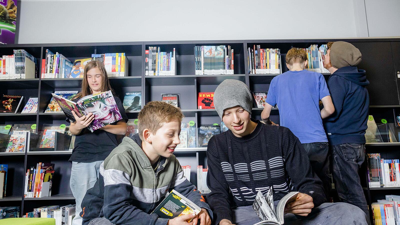 Junge und Jugendliche stehen oder sitzen in Zeitschriften-Ecke der Bibliothek mit Zeitschriften