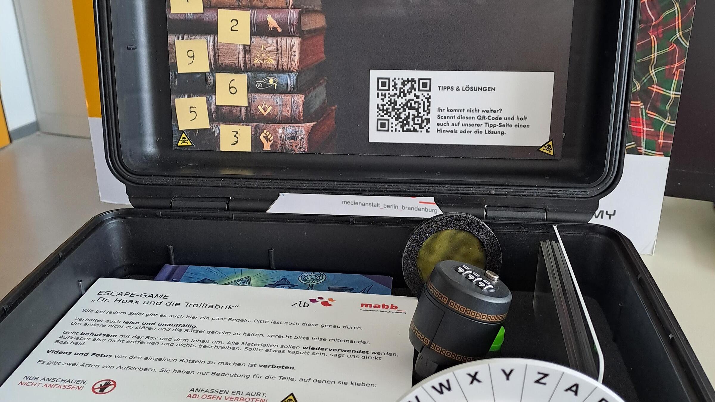 Foto vom Escape-Game-Koffe, der aufgeklappt Rätsel mit verschiedenen Bildern enthält.