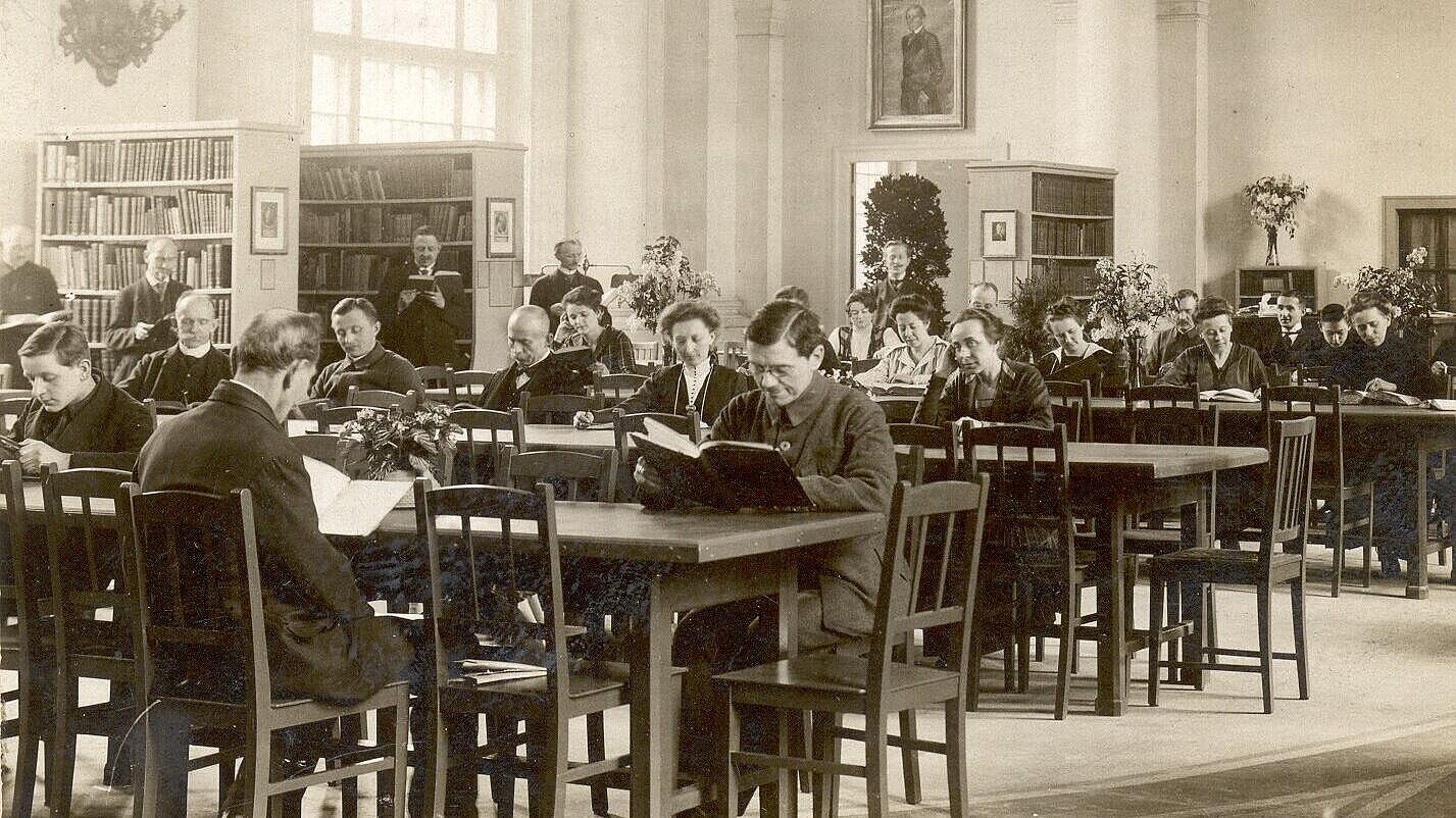 Historical photograph of people with opened books at long wooden tables in library