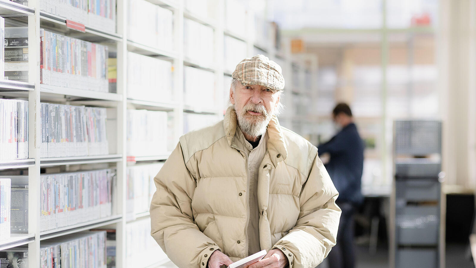 Elderly gentleman standing in front of shelf full of DVDs with DVD in his hands
