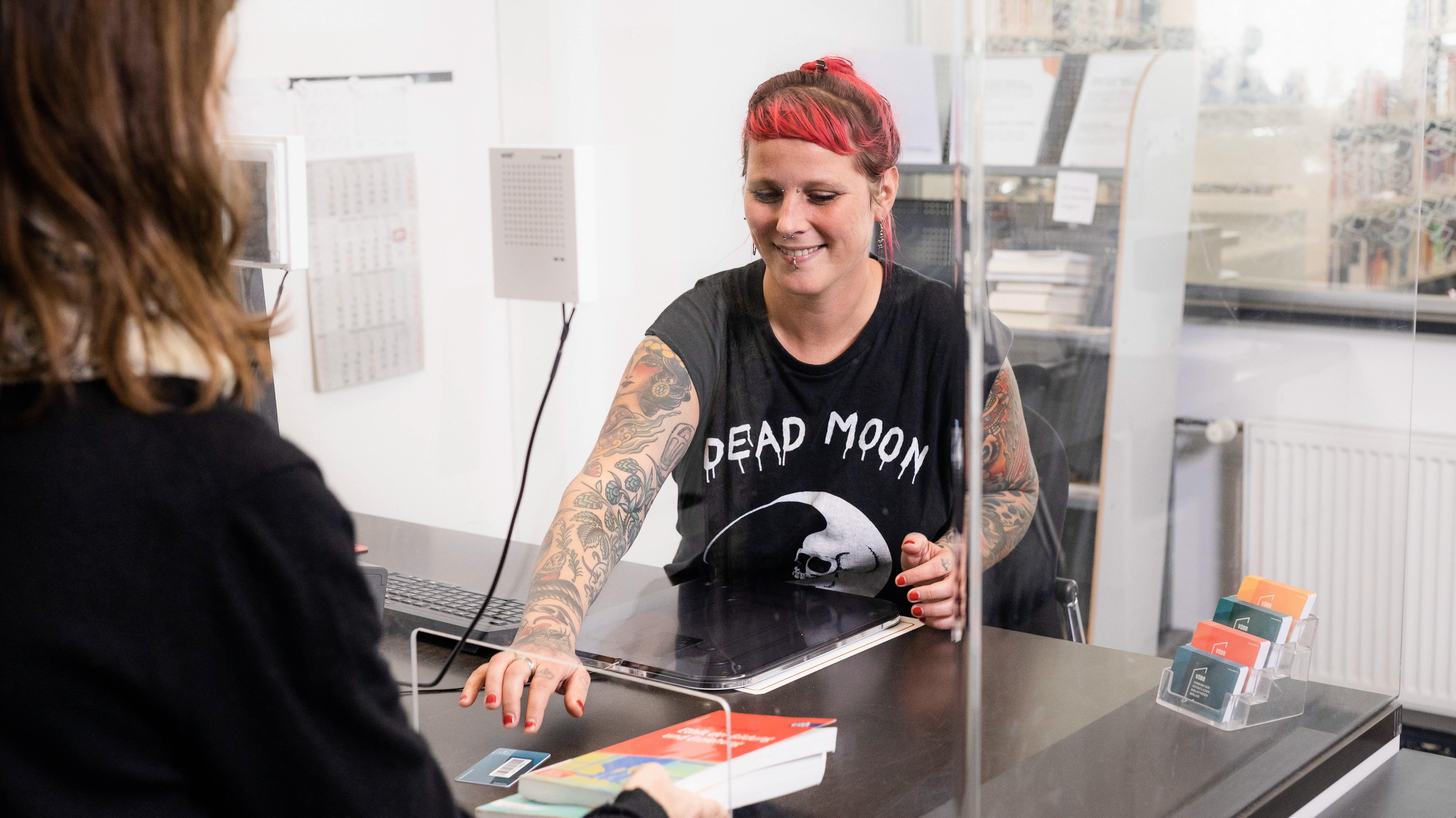 Foto von einer Person, die an der Servicetheke in der Bibliothek der Kundin die Bücher verlängert