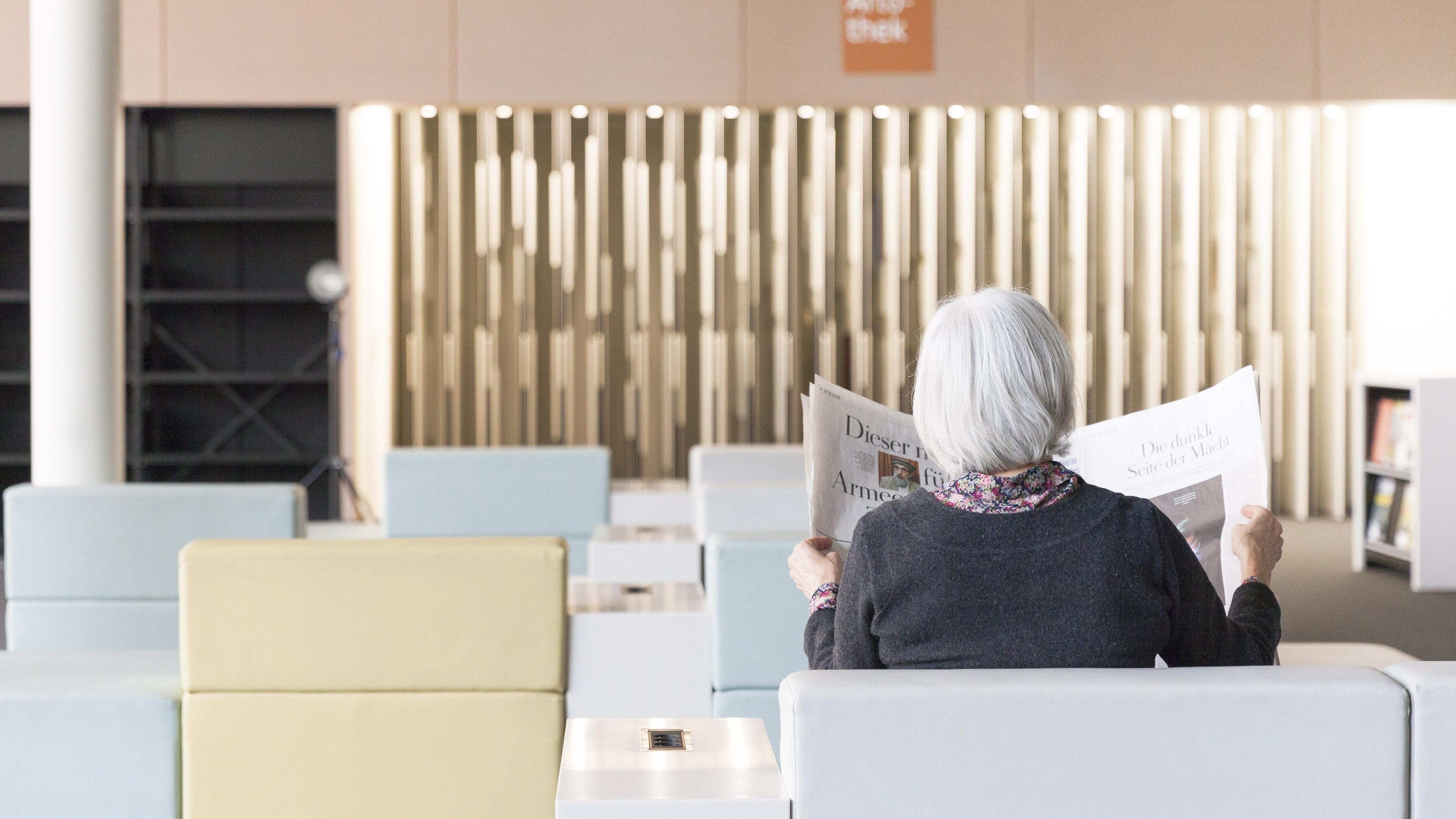 Frau mit Zeitung sitzt im Salon der AGB und liest Zeitung