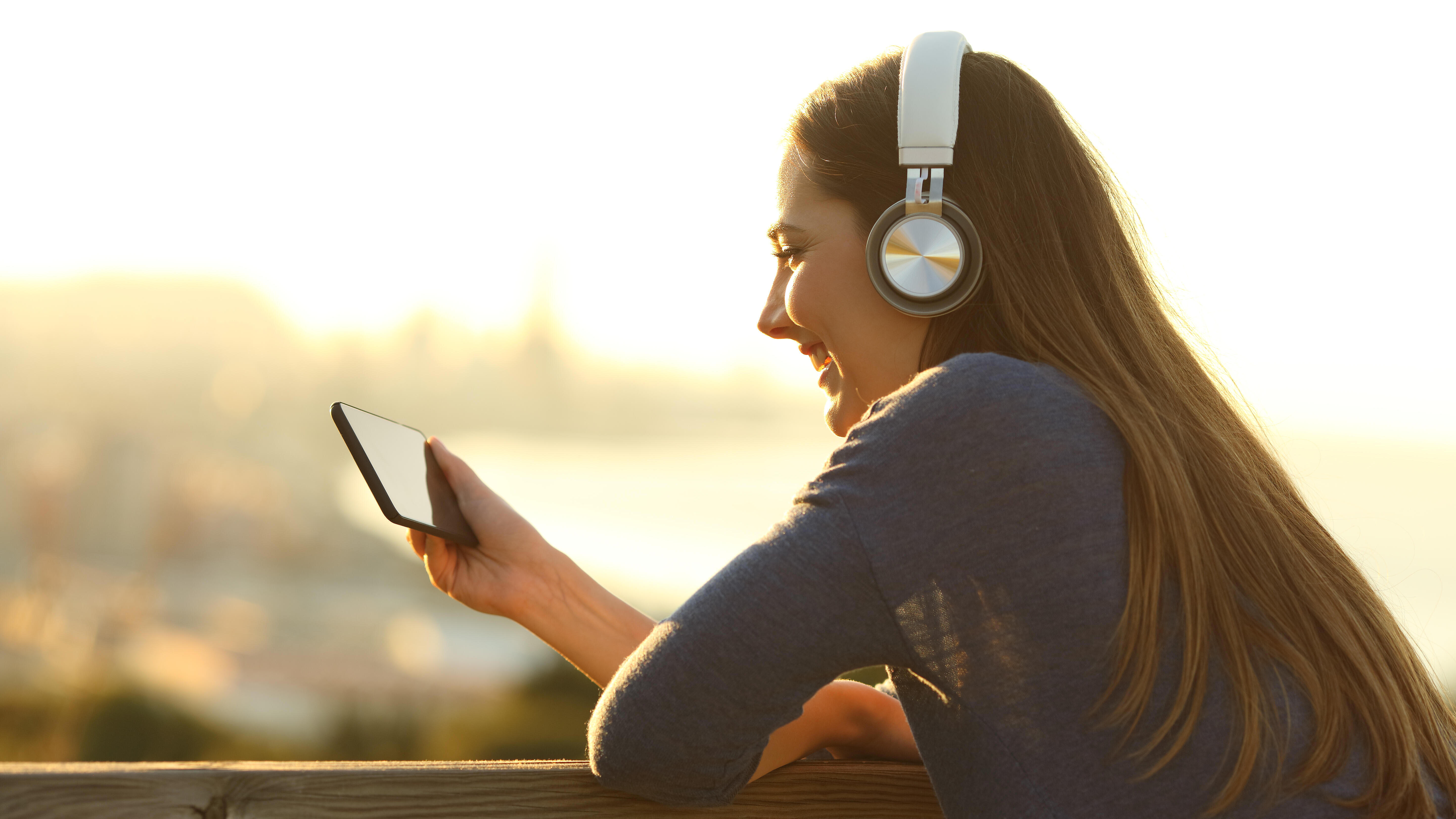 Junge Frau mit Kopfhörern schaut Videos auf Smartphone in der Sonne