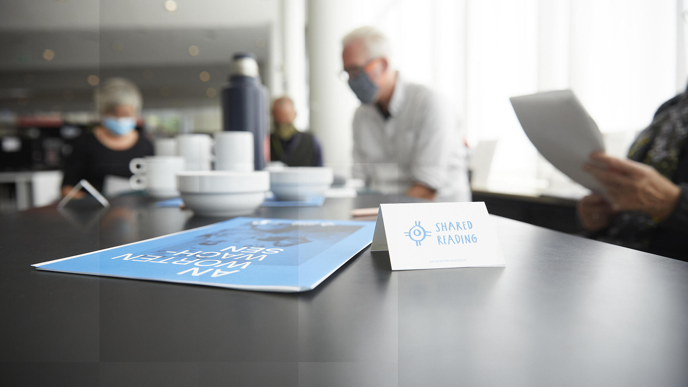 Table with "Shared Reading" display and people reading together in the background