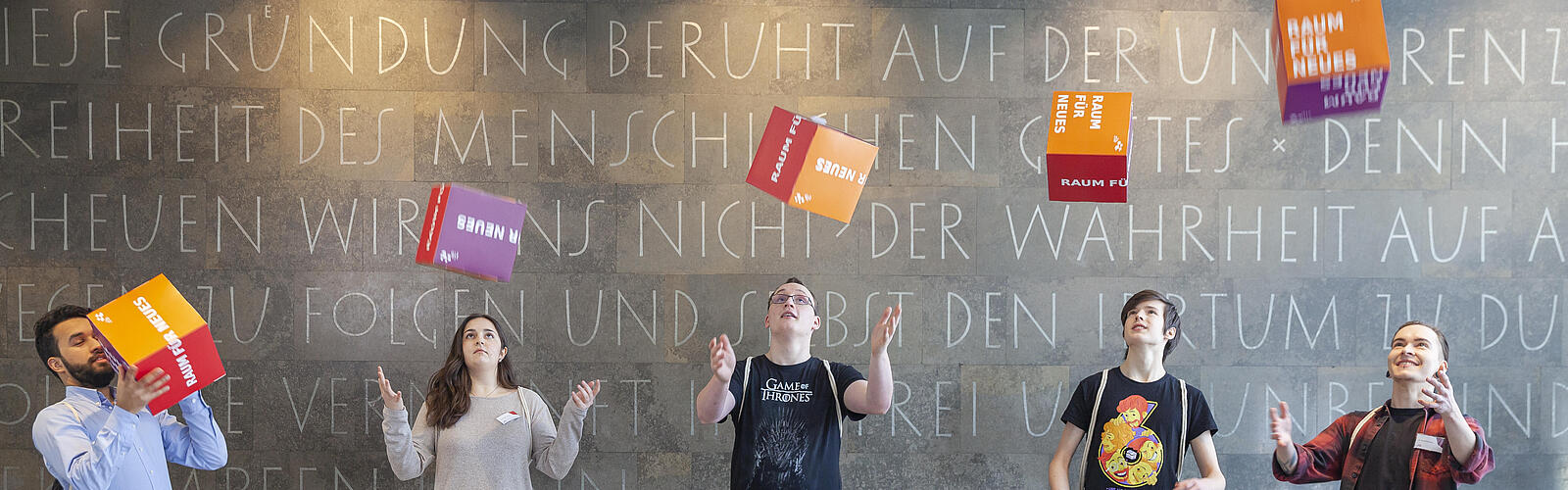 Auszubildende im Foyer der AGB werfen Pappwürfel mit der Aufschrift Raum für neues in die Luft