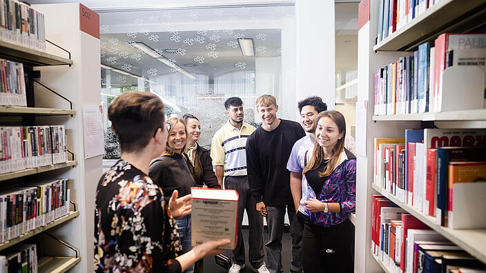 Eine Gruppe von Menschen steht vor Bücherregalen in einer Bibliothek.