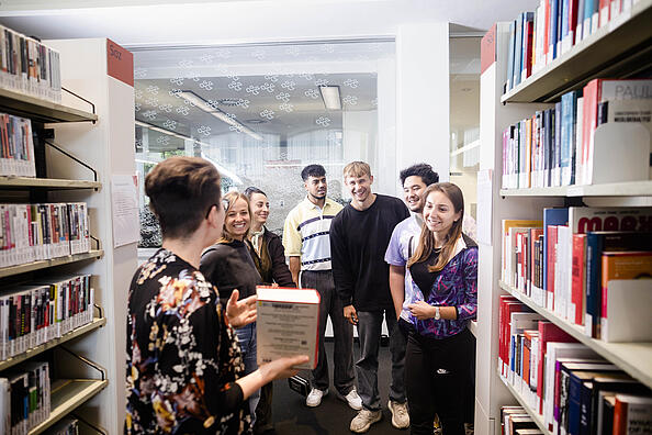 Eine Gruppe von Menschen steht vor Bücherregalen in einer Bibliothek.