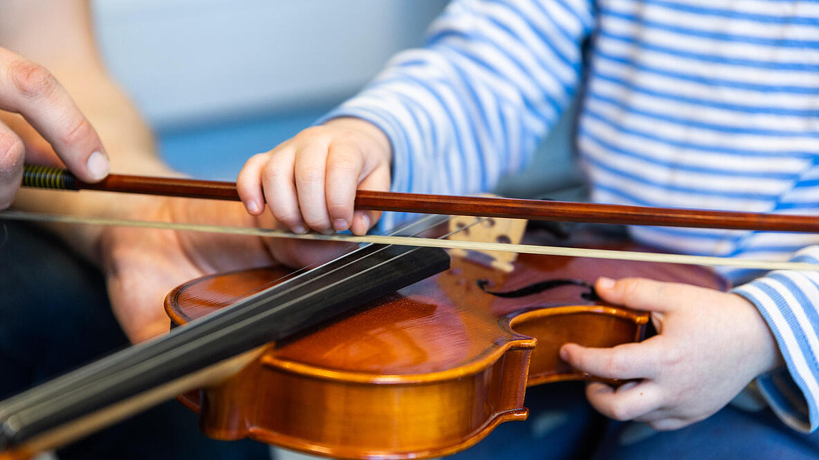 Kinderhände und Erwachsenenhände spielen zusammen Geige