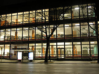 Die hell von innen beleuchtete Fassade der BStB von außen bei Nacht