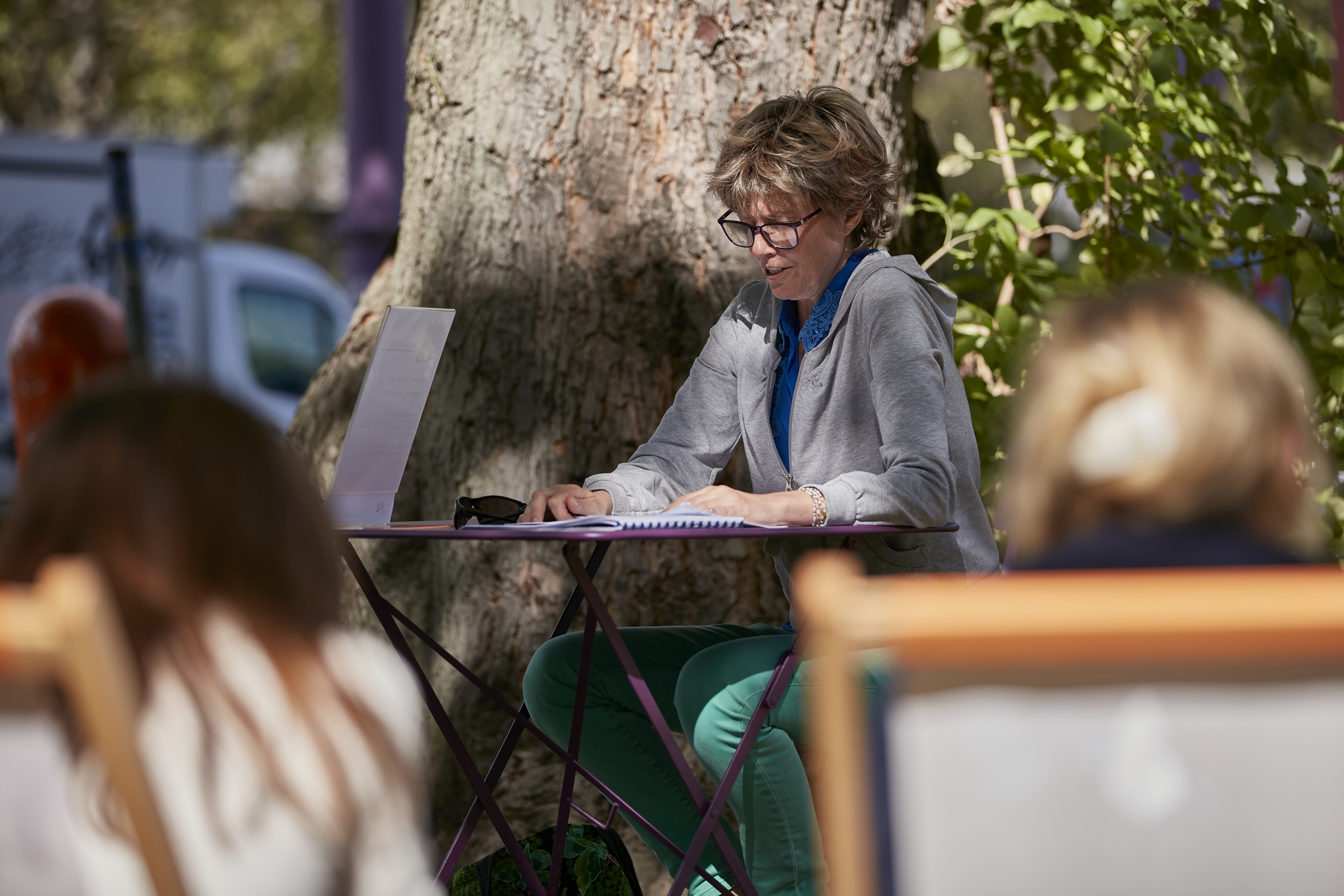 Autorin sitzt unter Baum vor der AGB und ließt aus einem Buch bei Veranstaltung